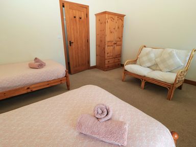 A bedroom with two single beds with folded towels a wooden wardrobe a wooden door and a two seat sofa with cushions at Keepers Cottage in Winterborne Stickland