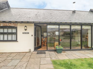 An exterior view of a building with a tiled roof a glass door and windows a plant in a pot on the patio at New Barn in Winterborne Stickland