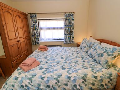A bedroom with a bed with patterned bedding and towels on it a wooden wardrobe and a window with curtains at New Barn in Winterborne Stickland
