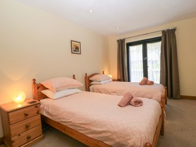 A bedroom with two single beds bedside tables and curtains at The Old Cart Shed in Winterborne Stickland