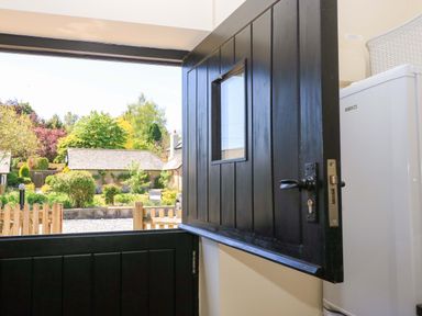 An open stable door with a window showing a garden and wooden fence at Rowdens Barn in Winterborne Stickland