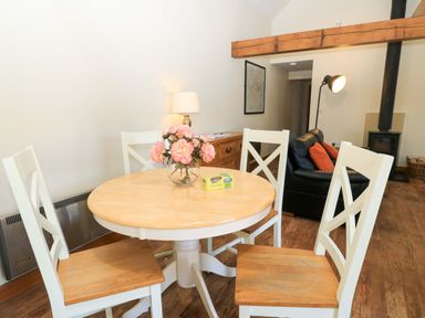 A dining area with a round wooden table and four white chairs with wooden seats at Rowdens Barn in Winterborne Stickland