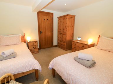 A bedroom with two single beds bedside tables a wooden wardrobe and a chest of drawers at Rowdens Barn in Winterborne Stickland