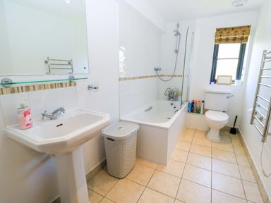 A bathroom with a pedestal sink soap dispenser laundry basket bathtub toilet and window at Rowdens Barn in Winterborne Stickland