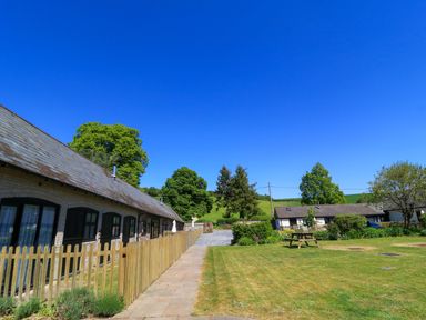 A courtyard with two single-story buildings separated by a lawn and a wooden picnic table at Rowdens Barn in Winterborne Stickland