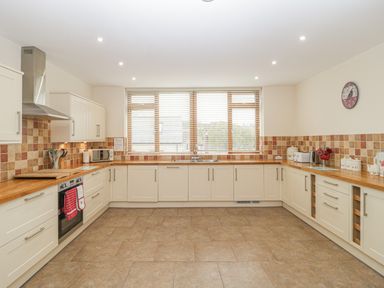 A kitchen with wooden countertops cabinets tiled backsplash and a window with blinds at The Old Barn in Harman's Cross near Swanage
