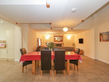 A dining area with six chairs and a polka dot tablecloth and a living room with a fireplace and a mounted TV at The Old Barn in Harman's Cross near Swanage