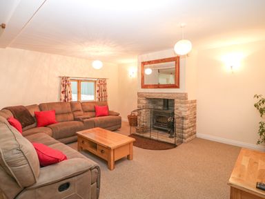 A living room with a sectional sofa red cushions a wooden coffee table stone fireplace and mirror at The Old Barn in Harman's Cross near Swanage