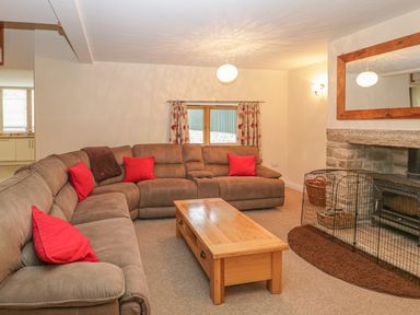 A living room with brown sectional sofa red cushions wooden coffee table and fireplace at The Old Barn in Harman's Cross near Swanage