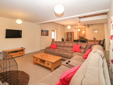A living room with sectional sofas red cushions wooden coffee table and a wall-mounted tv at The Old Barn in Harman's Cross near Swanage