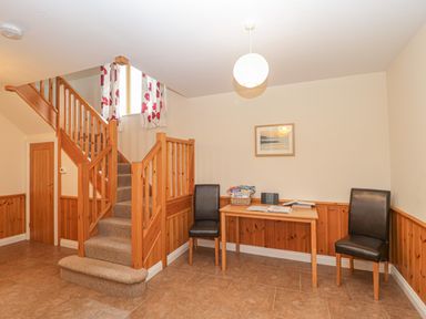 A hallway with a wooden staircase, two black chairs, and a wooden table at The Old Barn in Harman's Cross near Swanage