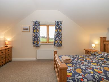 A bedroom with a wooden bed, two dressers, patterned curtains, and towels on the bed at The Old Barn in Harman's Cross near Swanage