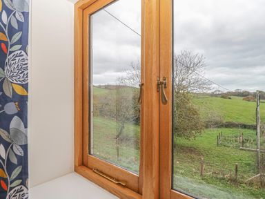 A window with wooden frame looking out to a green field with trees at The Old Barn in Harman's Cross near Swanage