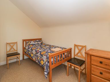 A bedroom with a single wooden bed with floral bedding two wooden chairs and a wooden chest of drawers at The Old Barn in Harman's Cross near Swanage