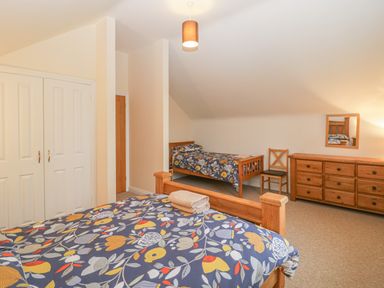 A bedroom with two wooden beds with patterned bedding a wooden dresser a chair and a closet at The Old Barn in Harman's Cross near Swanage