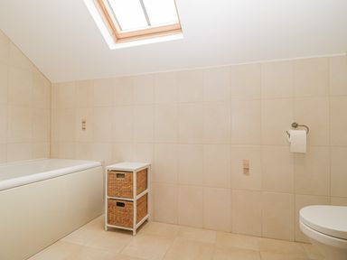 A bathroom with a bathtub a skylight a small storage unit and a toilet at The Old Barn in Harman's Cross near Swanage