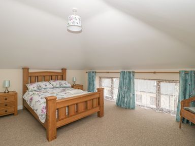 A bedroom with a wooden bed floral bedding two bedside tables with lamps blue curtains and a wicker chair at The Old Barn in Harman's Cross near Swanage