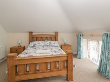 A bedroom with a wooden bed and bedside tables with lamps by a curtained window at The Old Barn in Harman's Cross near Swanage