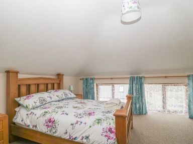 A bedroom with a wooden bed with floral bedding and folded towels near windows with blue curtains at The Old Barn in Harman's Cross near Swanage