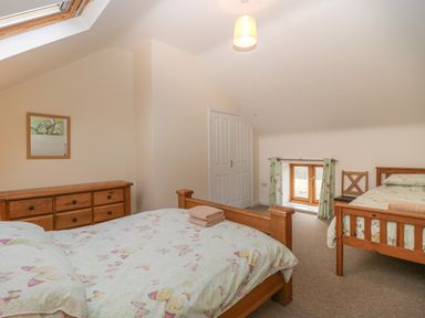 A bedroom with two wooden beds a wooden dresser a chair and a small window with curtains at The Old Barn in Harman's Cross near Swanage