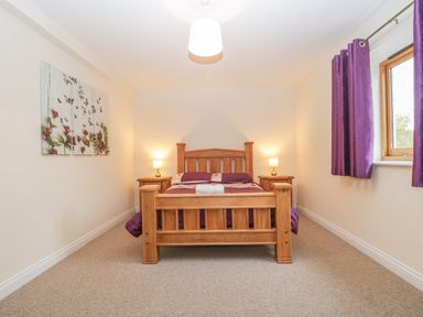A bedroom with a wooden bed, two bedside tables with lamps, purple curtains, and a floral wall art at The Old Barn in Harman's Cross near Swanage