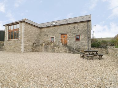 Stone building with steps leading to a wooden door and a picnic table on a gravel area at The Old Barn in Harman's Cross near Swanage