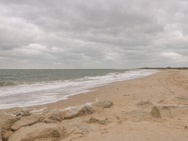 A sandy beach with waves and rocks under a cloudy sky at The Old Barn in Harman's Cross near Swanage
