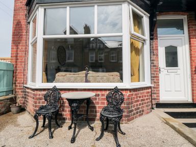 A brick exterior with two black metal chairs and a small round table in front of a large window at The Robins in Filey
