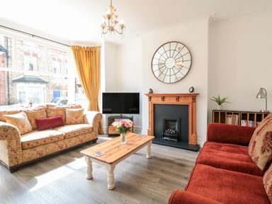 A living room with two sofas a coffee table a fireplace a TV and a large window with curtains at The Robins in Filey