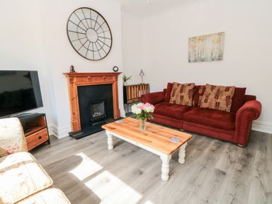 A living room with a red sofa a wooden coffee table flowers and a fireplace at The Robins in Filey