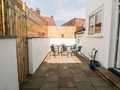 An outdoor patio area with a table and six chairs surrounded by wooden and brick walls at The Robins in Filey
