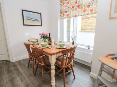 A dining table set with bowls plates and glasses with four wooden chairs by a window with floral blinds at The Robins in Filey