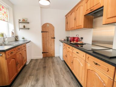 A kitchen with wooden cabinets a wooden door a stainless steel sink and countertop appliances at The Robins in Filey