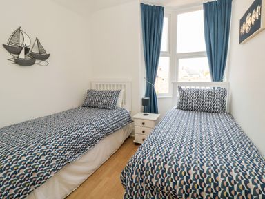 A bedroom with two single beds blue patterned bedding a small white bedside table and blue curtains at The Robins in Filey