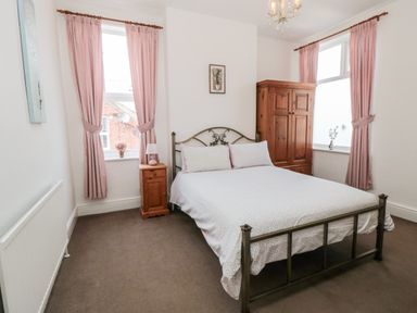 A bedroom with a double bed a wooden wardrobe and two windows with pink curtains at The Robins in Filey