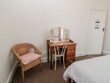 A bedroom corner with a wicker chair with a pillow a wooden dressing table with a triptych mirror and a chair next to a bed at The Robins in Filey