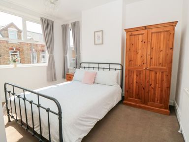 A bedroom with a metal bed frame a wooden wardrobe and windows with curtains at The Robins in Filey
