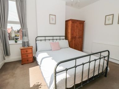 A bedroom with a metal bed frame a wooden wardrobe bedside table with lamp and window with grey curtains at The Robins in Filey