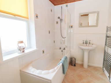 A bathroom with a bathtub and shower next to a window a sink and mirror at The Robins in Filey