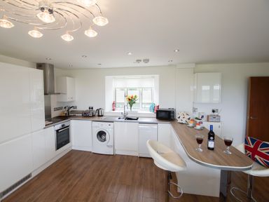 A kitchen with white cabinets wooden floor a washing machine and dishwasher at Beautiful Cotswold View in Bourton-On-The-Water