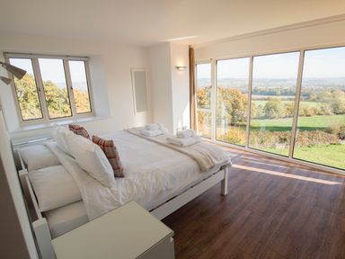 A bedroom with a bed beside large windows overlooking a green landscape at Beautiful Cotswold View in Bourton-On-The-Water