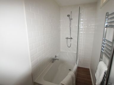 A bathroom with a bathtub shower combo white subway tiled walls a towel rail with towels and wood effect flooring at Beautiful Cotswold View in Bourton-On-The-Water