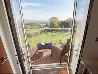 A balcony with two wicker chairs and a table overlooking a green field and trees at Beautiful Cotswold View in Bourton-On-The-Water