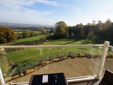 A balcony overlooking green fields and trees with a table holding a book and binoculars at Beautiful Cotswold View in Bourton-On-The-Water