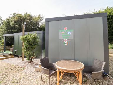An outdoor area with two modern grey buildings a round wicker table and two wicker chairs at Beautiful Cotswold View in Bourton-On-The-Water