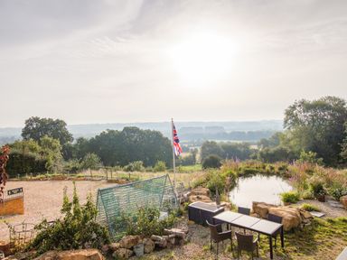 An outdoor area with a table and chairs by a pond with plants and a flagpole against a rural landscape at Beautiful Cotswold View in Bourton-On-The-Water