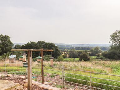 A countryside view with bird feeders hanging from a wooden post and metal railing at Beautiful Cotswold View in Bourton-On-The-Water