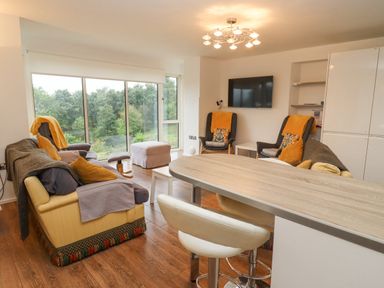 A living room with sofas and armchairs near large windows and a wall-mounted TV at Beautiful Cotswold View in Bourton-On-The-Water