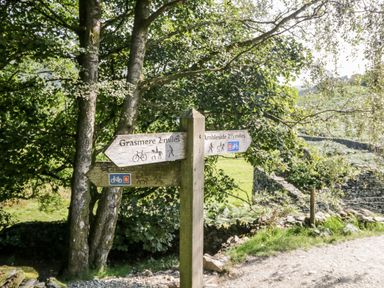 A wooden signpost with directions to Grasmere and Ambleside on a path surrounded by trees at Church View in Ambleside