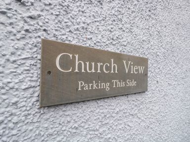 A close-up of a metal sign on a textured white wall reading Church View Parking This Side